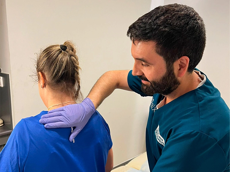 Fisioterapeuta realizando valoración manual de la columna a una paciente sentada en consulta del Centro DAX.